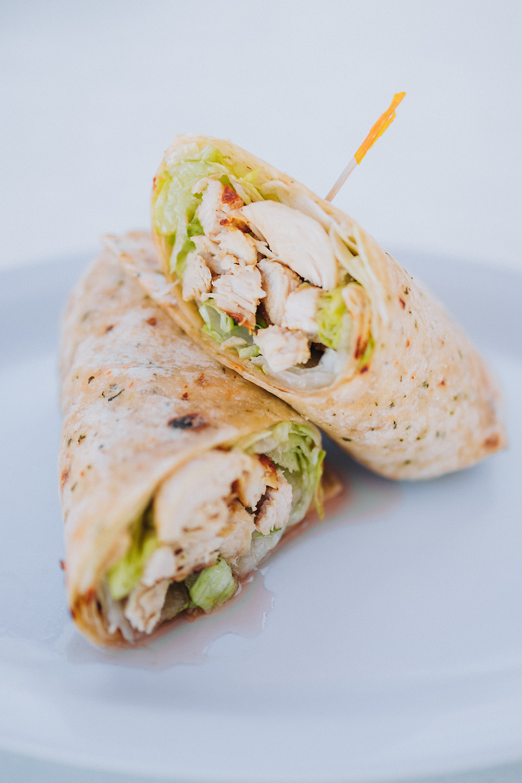 Grilled chicken wrap sliced in half showing chicken and lettuce on a white plate