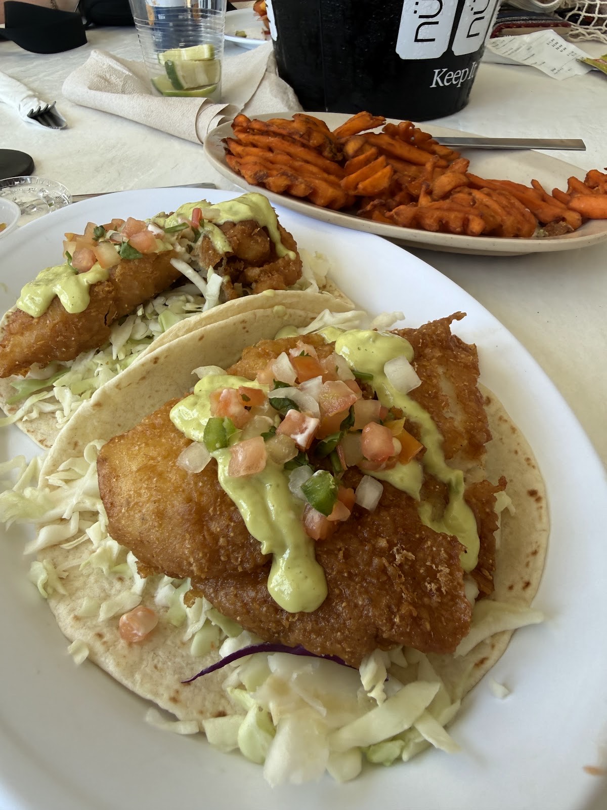 Two blackened fish tacos with avocado crema and pico beside a basket of sweet potato waffle fries