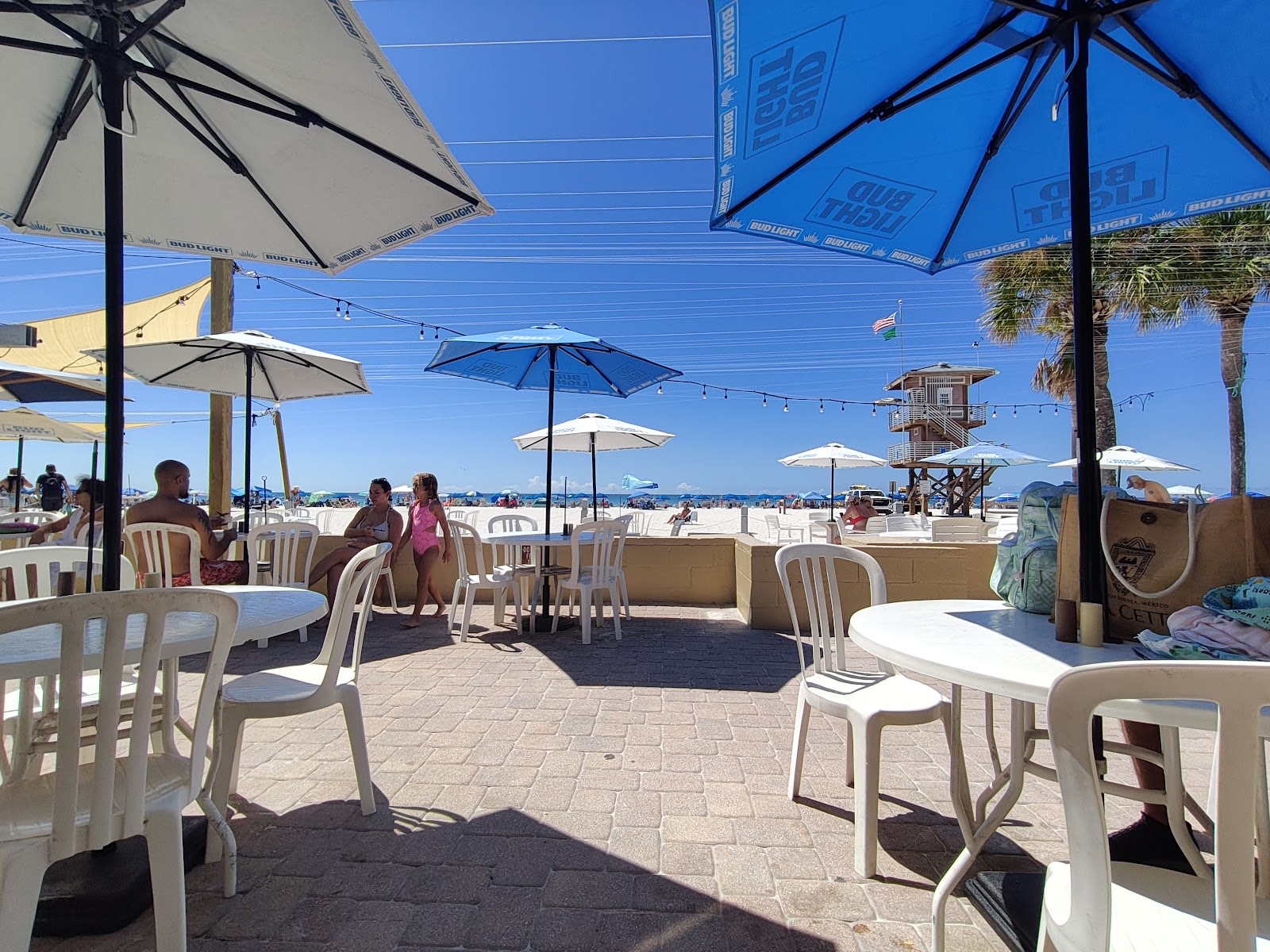 Beachfront tables and umbrellas in the sand at Anna Maria Island Beach Cafe with the Gulf and lifeguard tower behind